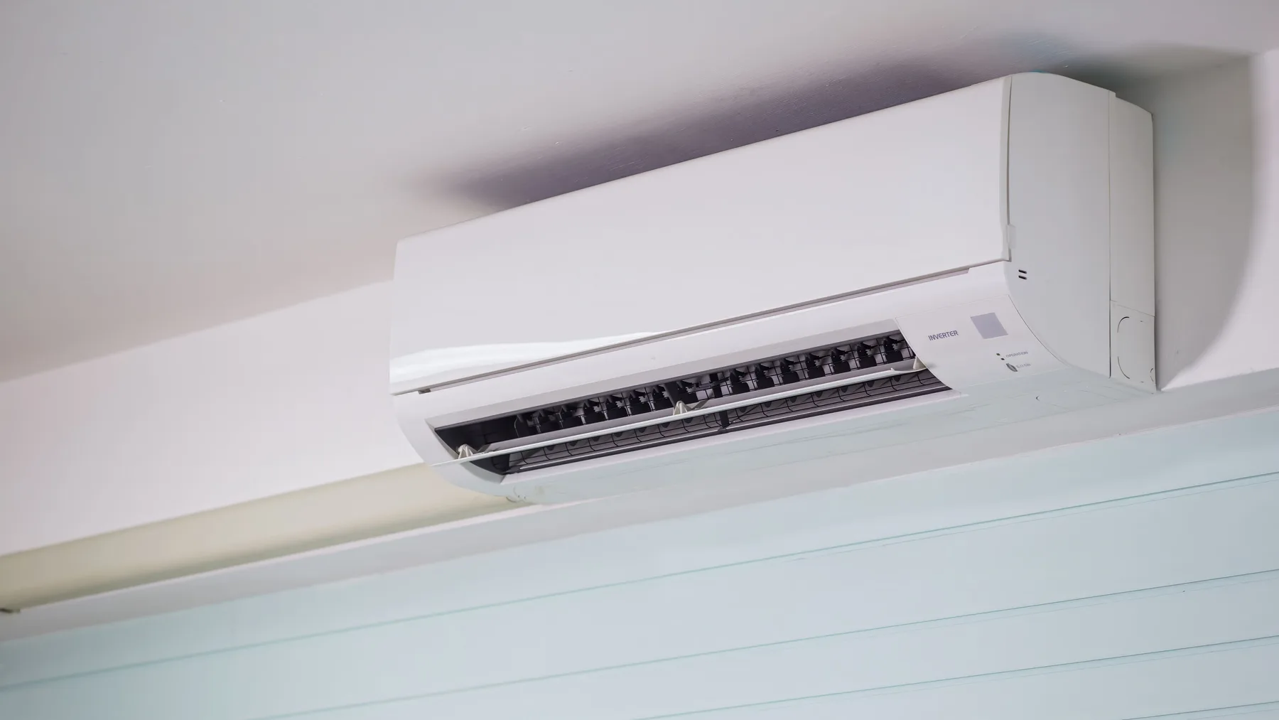 Wall-mounted split air conditioner indoor unit with its louvres open, fitted high on a plain white wall