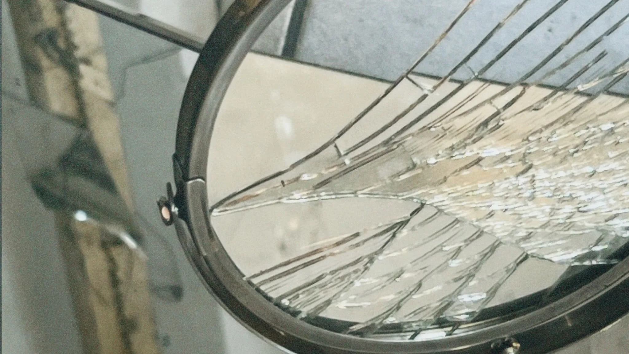 Round framed vanity mirror with its glass shattered into a fan of cracks and loose fragments