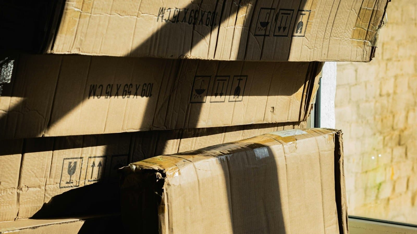 Stack of flattened cardboard boxes with shipping labels leaning against a wall in bright sunlight