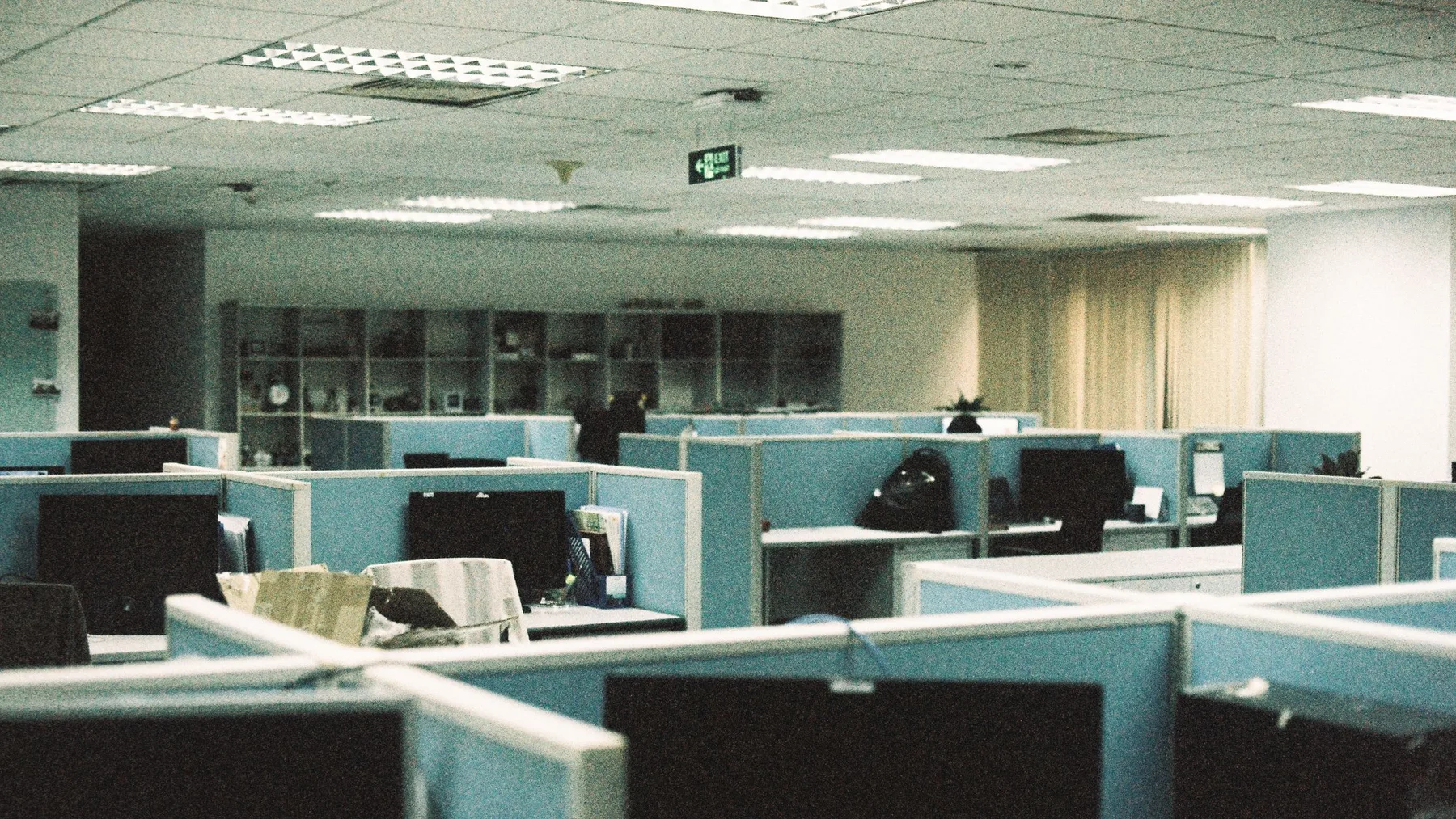 Open-plan office floor with rows of empty desks, fabric screen partitions and monitors left in place