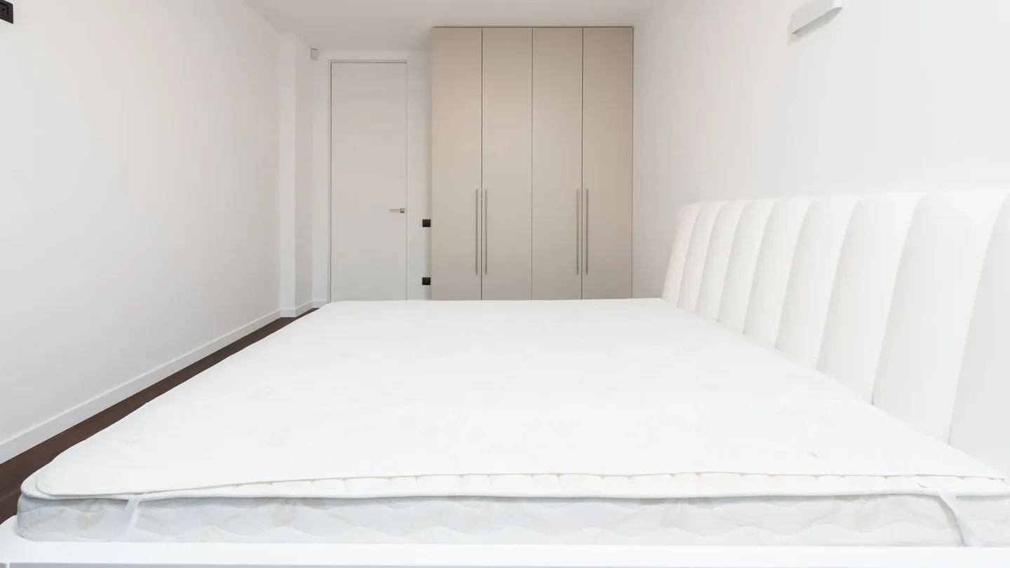 Small plain bedroom with a single mattress on a white bed frame and a built-in wardrobe beside the door