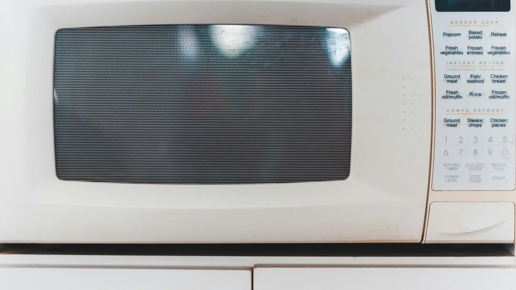 Front of an ageing white countertop microwave showing its mesh door screen and worn button panel