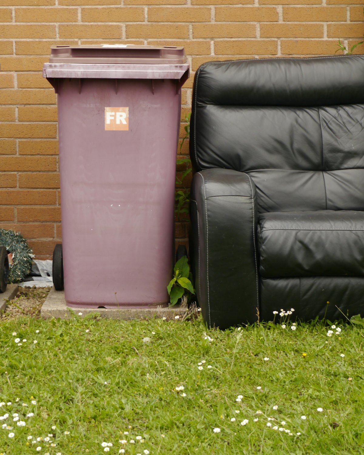 Discarded leather sofa and a wheelie bin left outside a home ready for bulky furniture collection